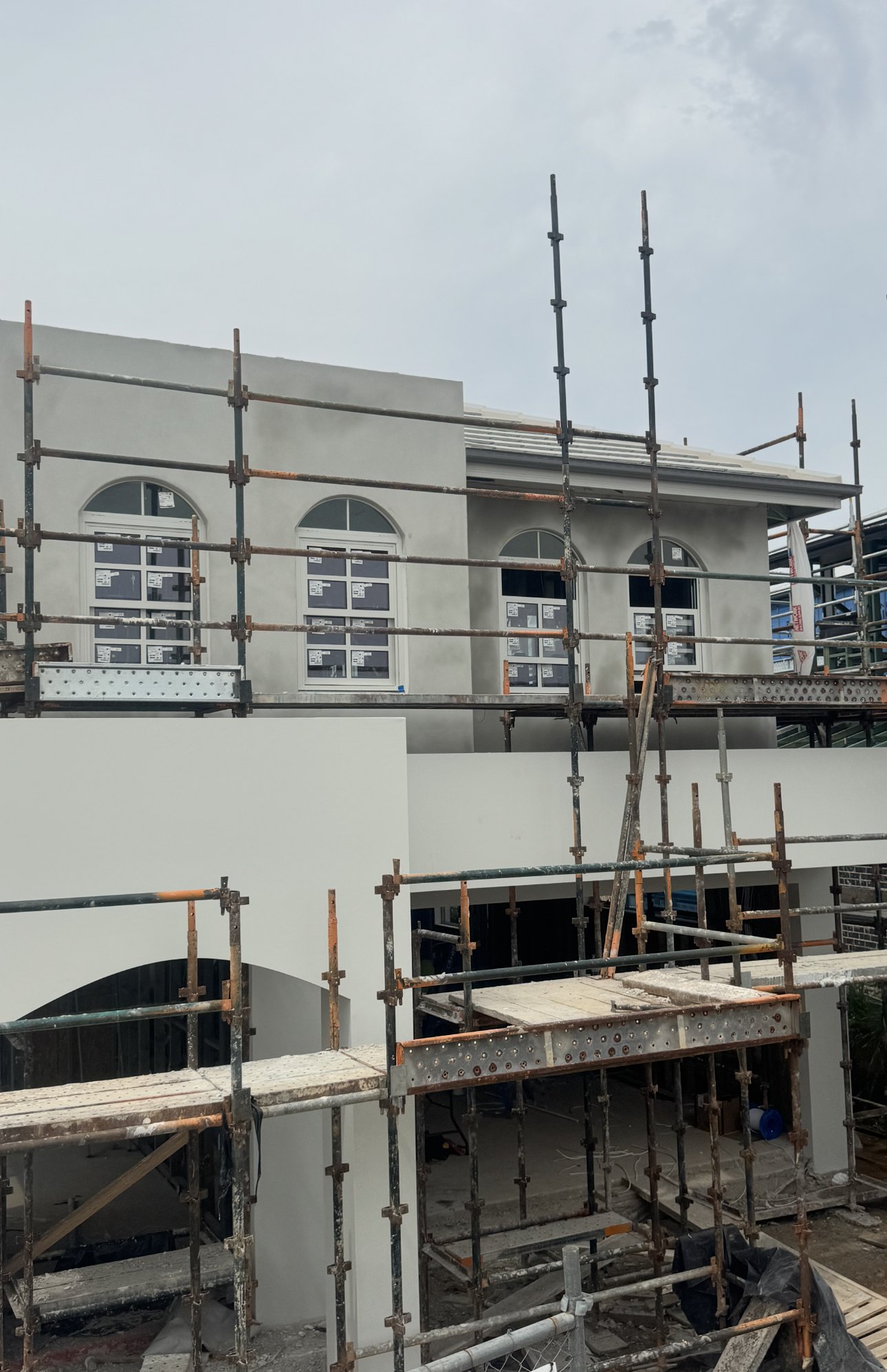 Larger home with arched windows being rendered, scaffolding across the front