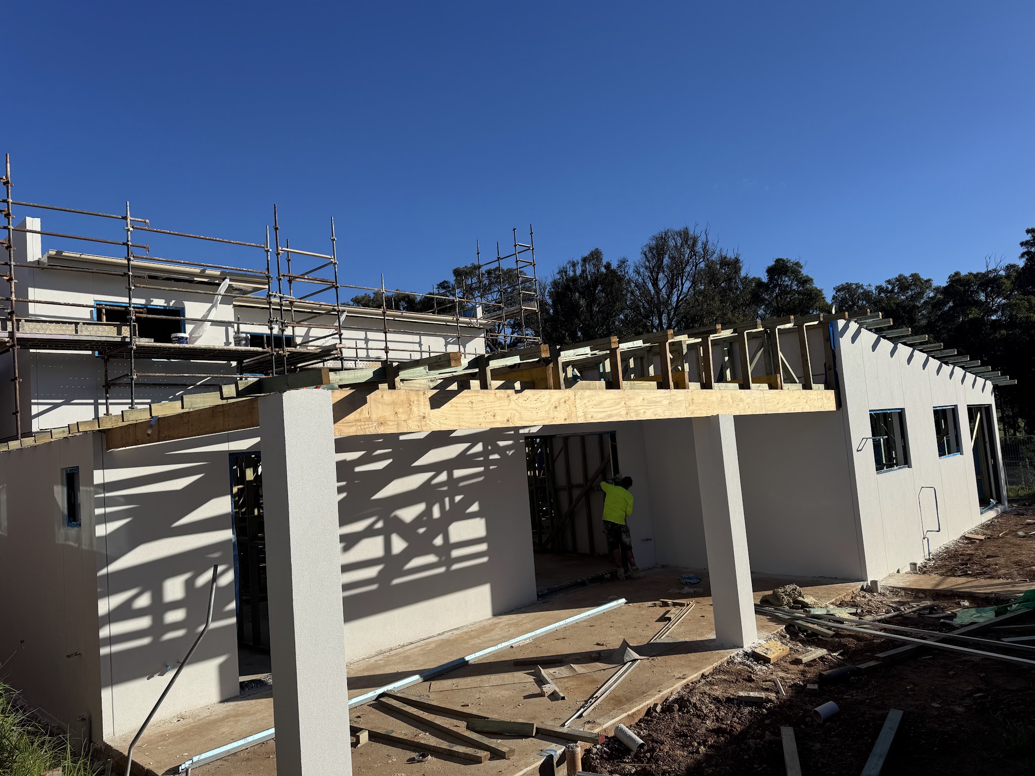 Rendered walls on a new build with the roof framing still going up and a worker in hi-vis