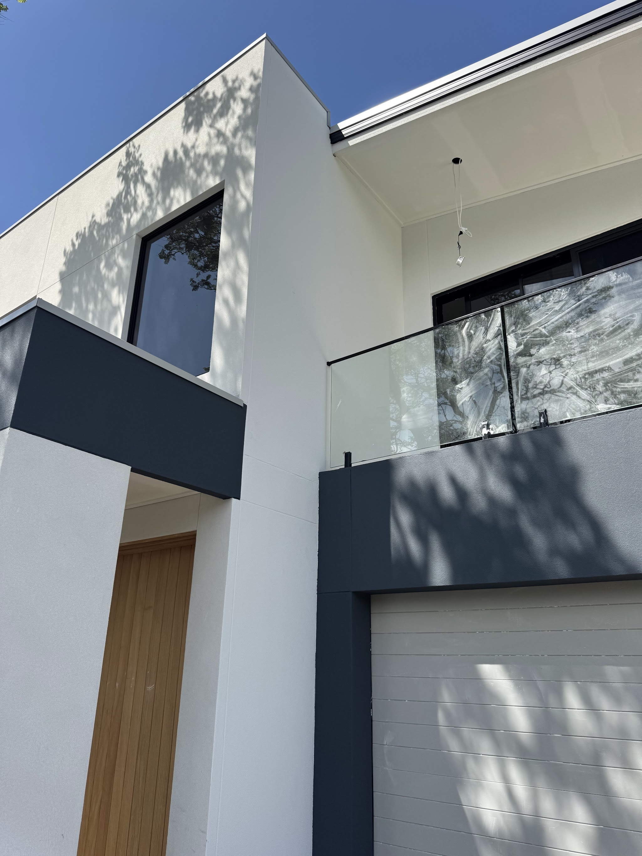 Close view of a white and charcoal rendered facade with a balcony and timber front door