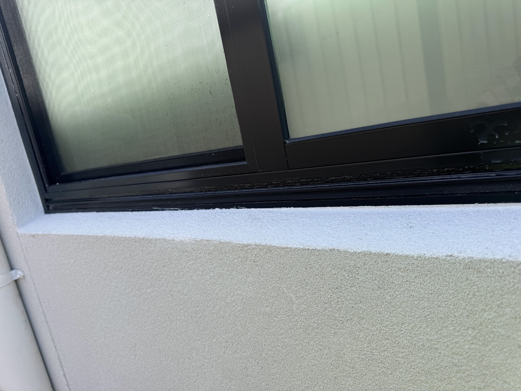 Close-up of a sand-textured rendered window sill below a black window frame